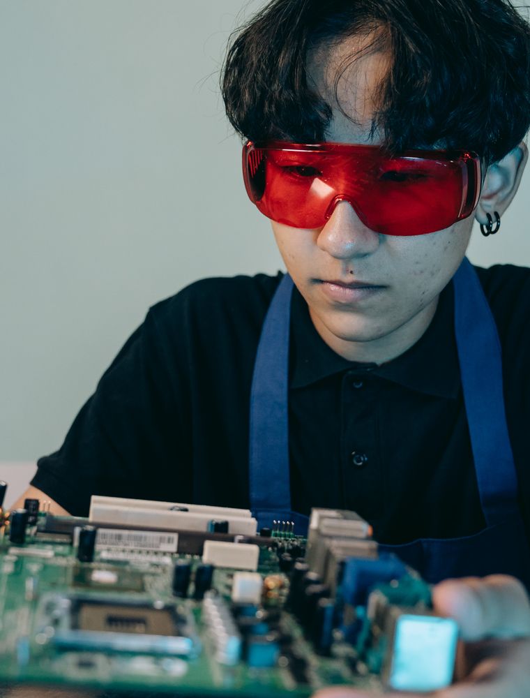 A teenager in safety glasses working on a circuit board